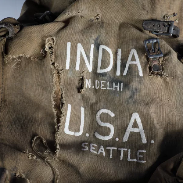A worn, torn backpack with INDIA NEW DELHI U.S.A. SEATTLE printed on the front. 