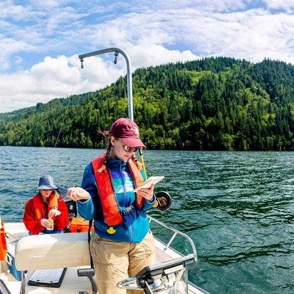 a student on a boat in the middle of Lake Whatcom consults their notes while conducting water quality testing. 