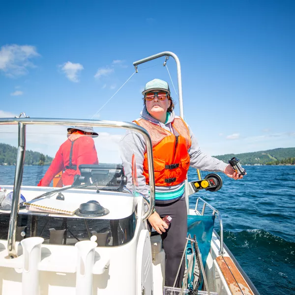 Two students on a boat in the middle of Lake Whatcom, one holds a tube preparing to take a water sample. 