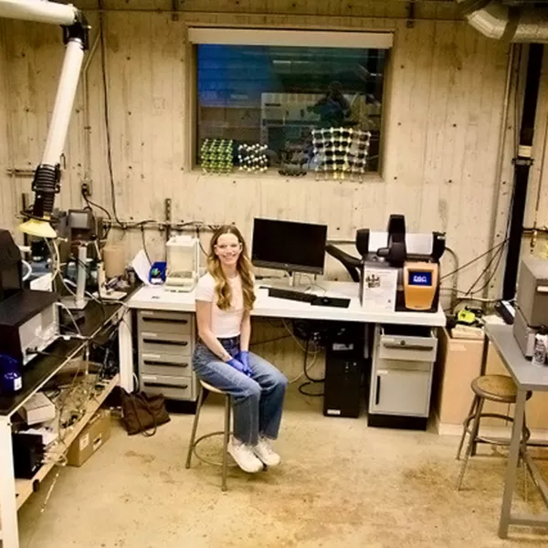 A student sits in the middle of a scientific laboratory, surrounded by equipment