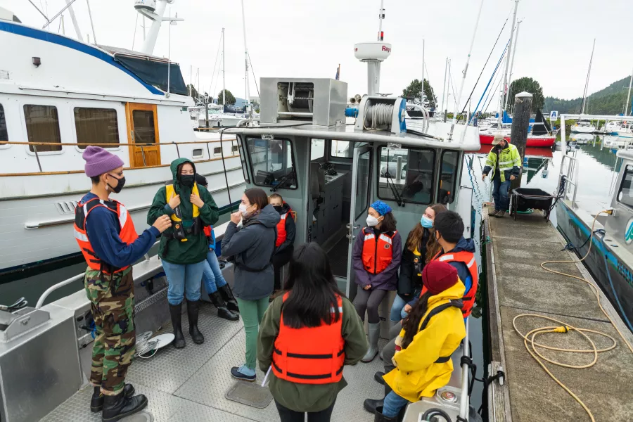 a group of students gather on the deck of a docked research boat