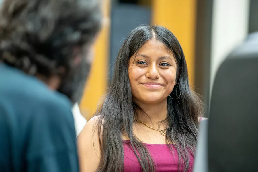 A student smiles as she listens to someone in the foreground. 