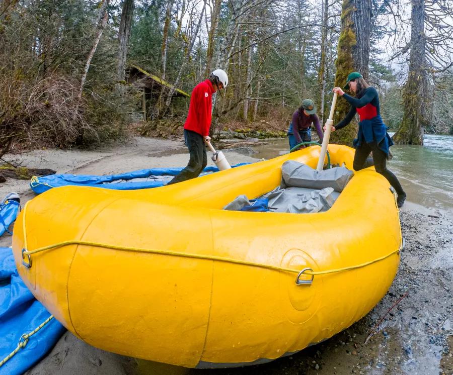 three students use cylindrical hand pumps to inflate a river raft