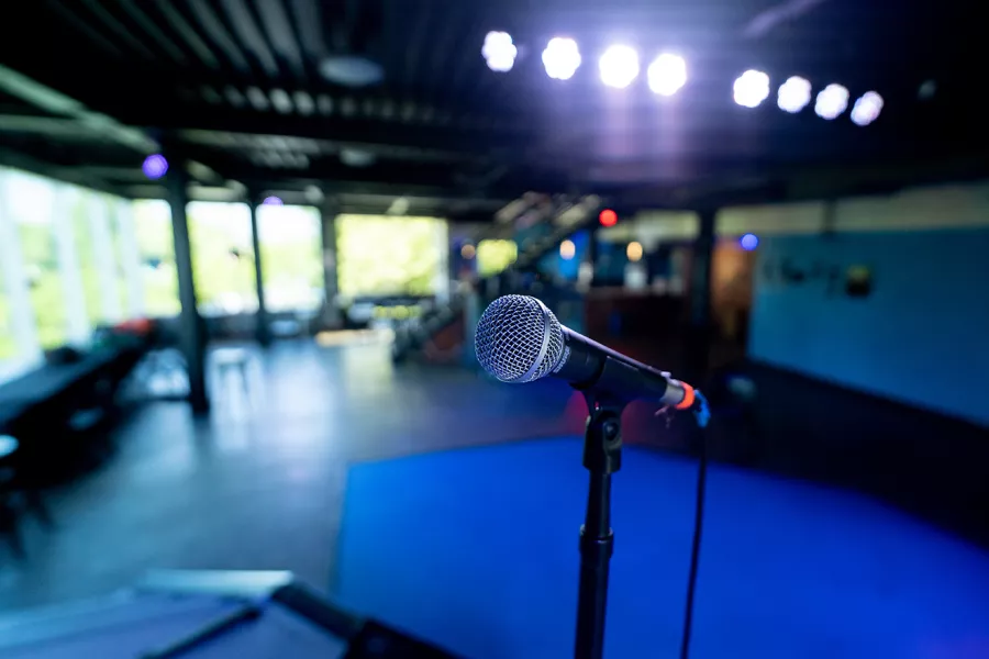 a microphone sits on an empty stage, an empty performance venue in the background.