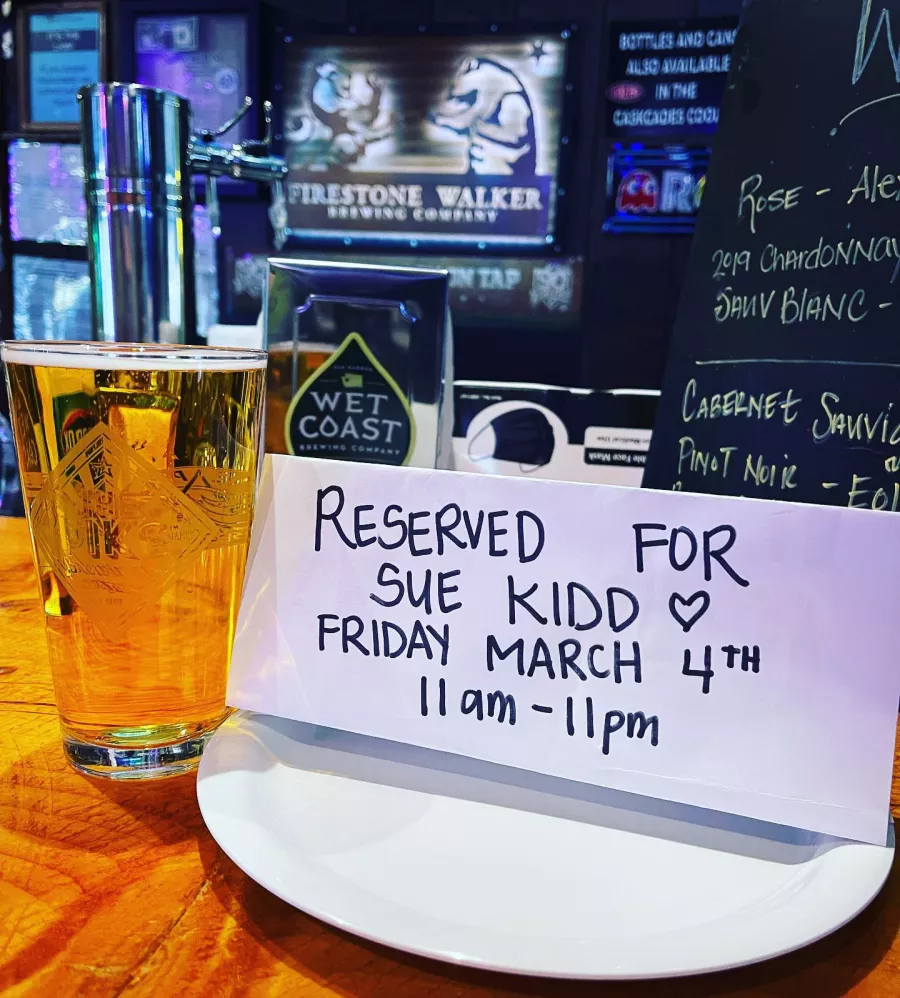 A pint of beer sits next to a hand-printed sign Reserved for Sue Kidd Friday March 4th 11 am-11pm