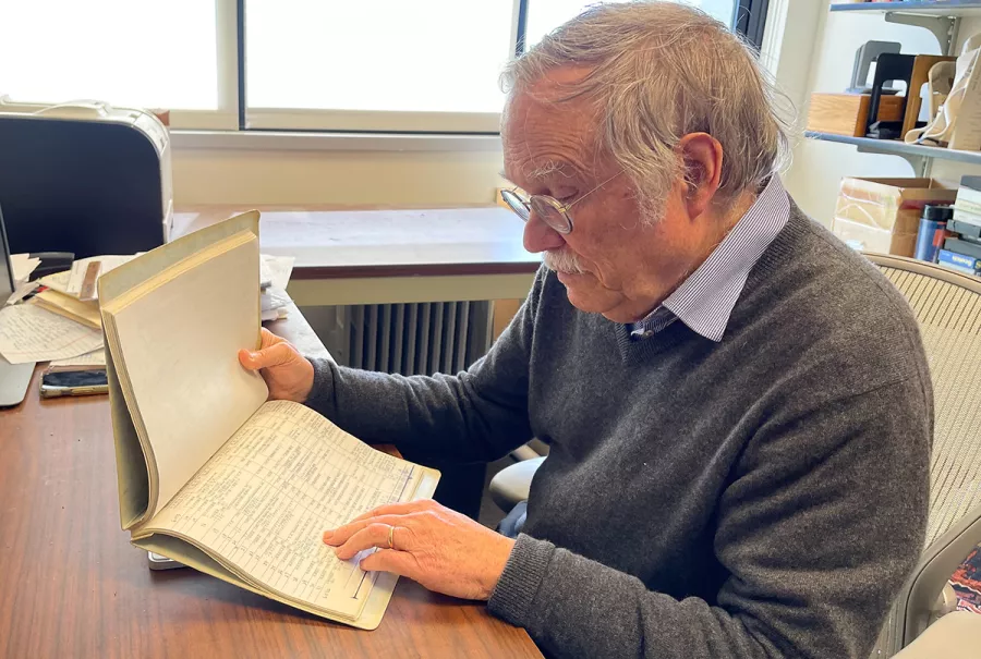 Tom Roehl sits at a desk looking at a ledger book. 