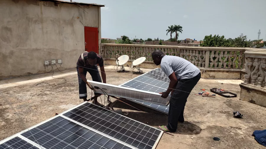 Two men carefully place a solar panel in an array on a sunny balcony atop a house in Benin. 