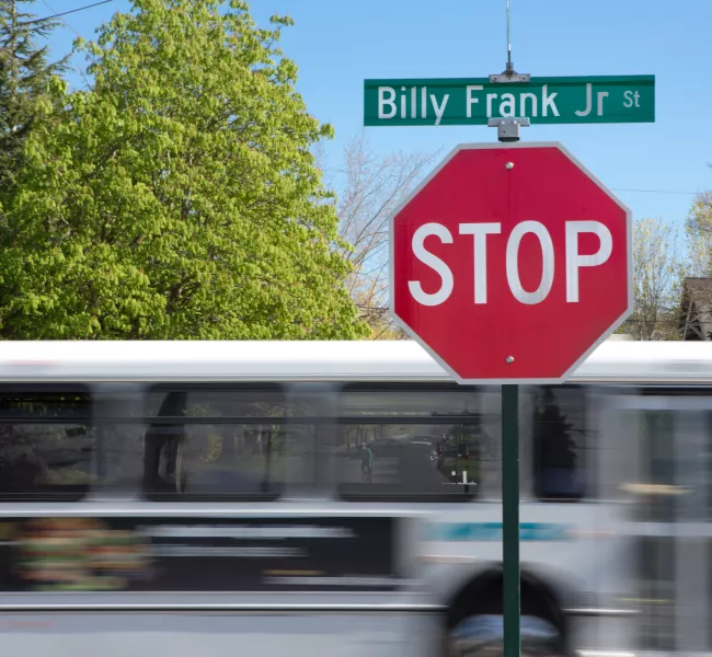 A bus passes a stop sign with a street sign atop: Billy Frank Jr. St.