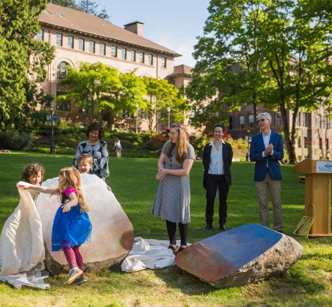 AS Child Development Center kids  Nox Tuigamala, Ivie Gilbert, and Calder Amos remove the coverings from  “Split Stone (Northwest)” during the  sculpture’s unveiling ceremony in May. Watching are several adults including artist Sarah Sze.