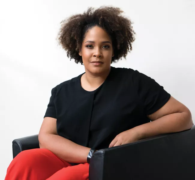 Ijeoma Oluo sits in a modern arm chair, facing the camera 
