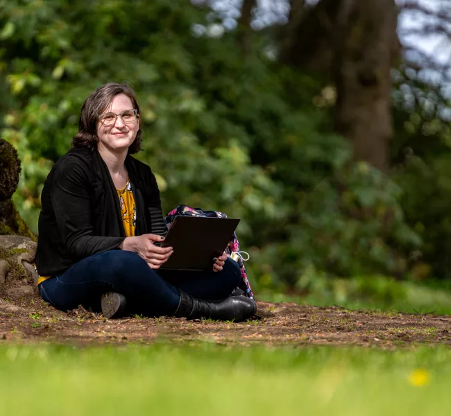 Caitlin Bannister sits beneath a tree on campus, a laptop computer in her lap