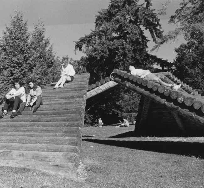 Students sit and lie down on the sloping stacked logs of the Log Ramps sculpture