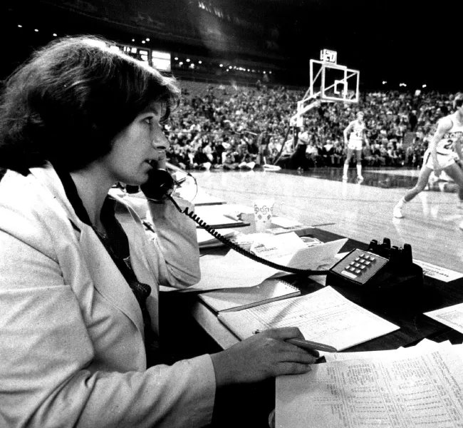 A woman sits at a table and talks on a corded telephone while at courtside during a professional basketball game