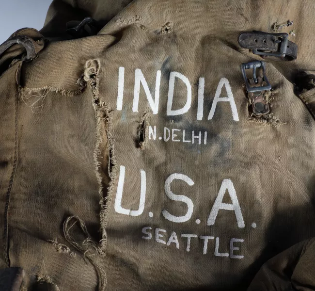 a worn, torn backpack with INDIA N. DELHI U.S.A. SEATTLE printed on the front. 