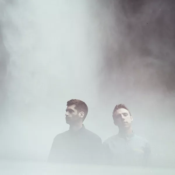 The members of Odesza stand before a waterfall. 